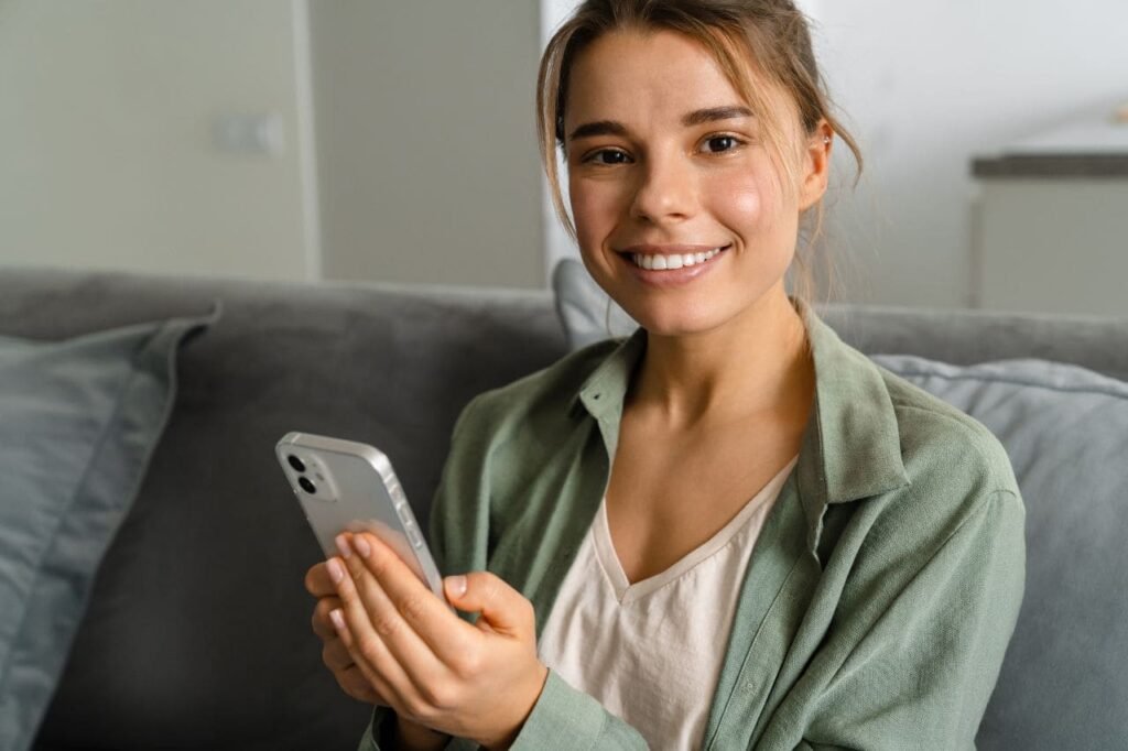 Individuell Das Bild zeigt eine zufriedene Frau, die ihr Smartphone in der Hand hält und in die Kamera schaut.